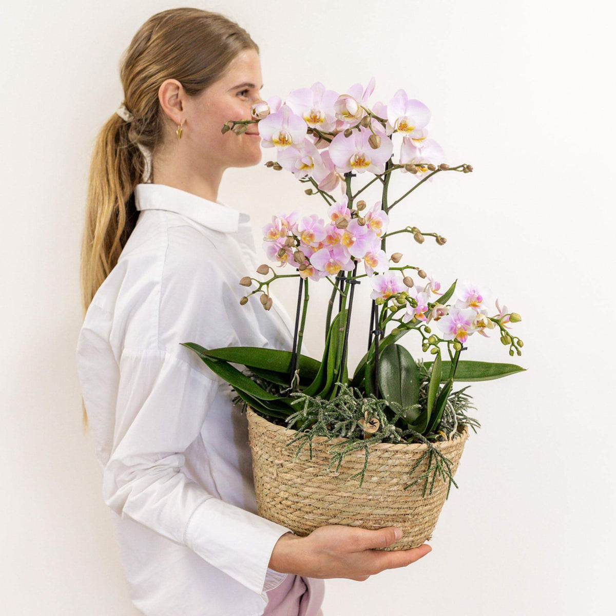 Vrouw met roze Kolibri Orchids en groene planten in een katoenen mand met waterreservoir, prachtig Field Bouquet.