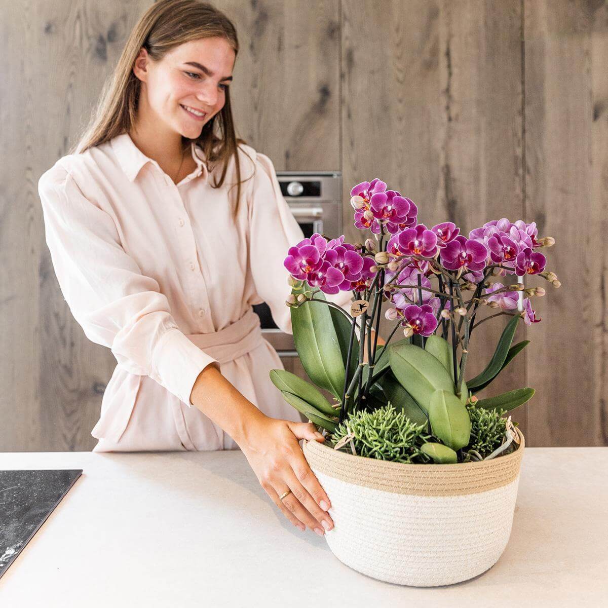 Vrouw met paarse orchideeën set in katoenen mand met waterreservoir op aanrecht