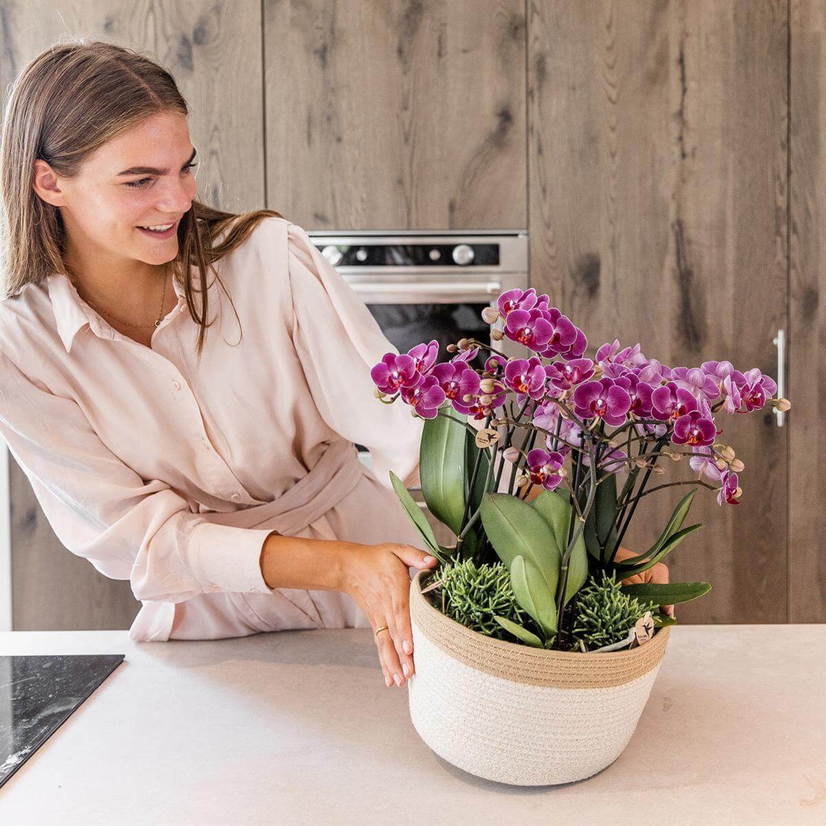 Vrouw met paarse Kolibri Orchids in witte katoenen mand met waterreservoir, in moderne keuken.